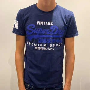 Blå Superdry t-shirt med tryck - Mörkblå vintage t-shirt från Superdry med stort blått och vitt tryck framtill och texten 'JPN' på ärmen. Storlek S. Nypris 700kr vårt pris 400kr. Tveka inte på att ställa frågor!