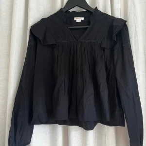 Svart blus med volang från Gina Tricot - svart blus från Gina Tricot med volangdetaljer på axlarna och spetsband över bröst och ärmar. 