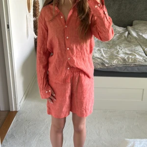 Korallfärgad linneskjorta Stenströms med shorts till från Stenströms - Snygg korallfärgad skjorta från Stenströms i storlek 34, tillverkad i mjukt linne. Skjortan har klassisk krage, långa ärmar med manschett och vita knappar framtill. Perfekt för dig som gillar en chill och fräsch stil under varmare dagar. även shorts som är korallfärgad ett perfekt sett till sommaren