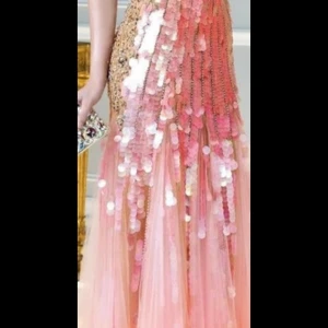 Lång rosa paljettklänning - Säljer en magisk långklänning i rosa och champagne med stora paljetter och transparent tyll. Klänningen har en glamorös look med glittriga detaljer som faller snyggt längs kjolen. Perfekt för dig som vill sticka ut på bal eller fest! Funkar för de som har XS 