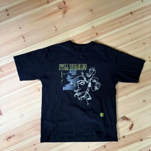 Svart t-shirt med grafiskt tryck - Svart t-shirt med coolt grafiskt tryck framtill i vitt och gult, där det står 'STILL DREAMING' och har abstrakta ansikten. Klassisk passform och rund hals. Perfekt för dig som gillar streetstyle och unika prints.