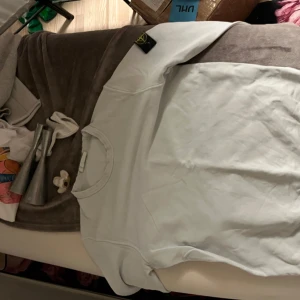 Baby blue sweatshirt från Stone Island - Säljer en clean baby blue sweatshirt från Stone Island med klassisk rund hals och den ikoniska logotypen på vänster ärm. Tröjan har lång ärm och är gjord i mjuk bomull, perfekt för chill dagar. Enkel och stilren design som funkar till jeans eller joggers.