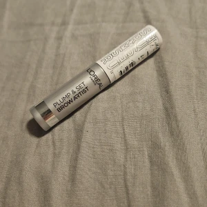 L'Oréal Plump & Set Brow Artist - L'Oréal Plump & Set Brow Artist är en ögonbrynsgel i en smidig tub med silverfärgad design. Perfekt för att forma och fixera brynen med ett naturligt resultat. Enkel att applicera och ger brynen extra volym och stadga.