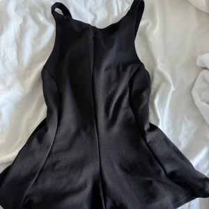 Svart peplumtop med knyt XS - Snygg svart peplumtop i slät polyester med breda axelband och knyt i ryggen. Toppen har en figurnära passform upptill och volangig peplum nedtill som ger en cool siluett. Perfekt för dig som gillar stilrena och trendiga plagg.