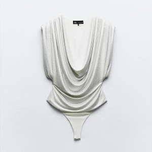 Glittrig silver bodysuit från Zara - Supersnygg glittrig silverfärgad bodysuit från Zara med djup draperad v-ringning och ärmlös design. En perfekt fest topp! Toppens material är glittrigt och stretchigt syntet, perfekt för att sticka ut. Sitter tajt och har en riktigt cool partykänsla. Finns inte kvar på hemsidan, har inte använt, prislappen sitter kvar. Köpt för 700 kr💞
