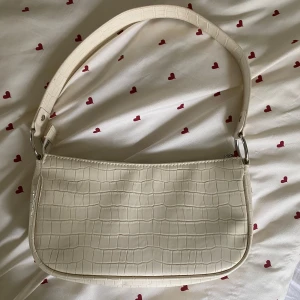 Väska - Säljer en vit/cremefärgad axelväska från H&M Divided med krokodil mönstrad yta. Väskan har en bred axelrem, silverfärgade metalldetaljer och stängs med dragkedja. Perfekt storlek för det viktigaste och ger en clean vibe till din outfit!💕Supersnygg som passar till allt😻Fungerar också som handväska!