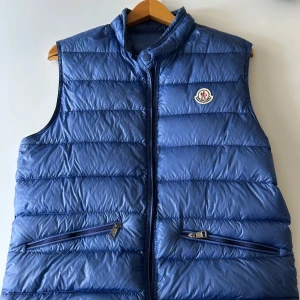 Moncler gui down vest(storlek 2) - Snygg blå dunväst från Moncler med quiltad design och hög krage. Västen har två dragkedjefickor framtill och klassisk Moncler-logga på bröstet. 