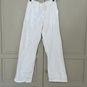 Vita linnebyxor från Gina Tricot - Snygga och luftiga vita linnebyxor från Gina Tricot med dragsko i midjan. Byxorna har raka ben och elastisk midja för extra komfort. Perfekta för varma dagar när du vill ha en chill och stilren look. Har en liten orange fläck