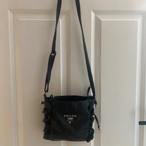 Svart axelväska - Vintage snygg svart axelväska i skinn med elegant snörning på sidorna. Väskan har en justerbar axelrem. Perfekt för att ge din outfit en lyxig touch.