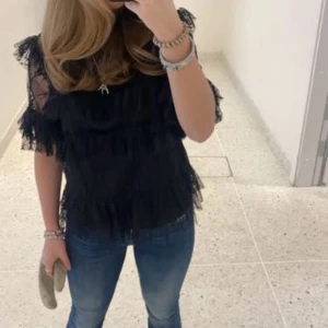 Svart spetsblus - Snygg svart blus med spetsdetaljer på ärmar och överdel. Blusen har korta ärmar och en elegant design som passar perfekt för en stilren look. Perfekt för att klä upp en outfit med en touch av spets.