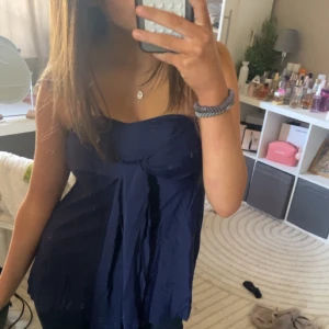 Mörkblå axelbandslös topp - Snygg mörkblå axelbandslös topp med knytning framtill. Perfekt för en somrig look. Toppen har en luftig passform och är tillverkad i ett lätt material.