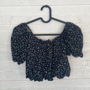 Svart blommig topp från Gina Tricot young 146/152 - Säljer en söt svart topp med vita blommor från Gina Tricot. Toppen har puffiga ärmar och en elastisk kant vid midjan för en bekväm passform. Perfekt för en somrig look! 🌸
