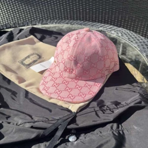 Rosa keps från Gucci - Snygg rosa keps från Gucci med det ikoniska GG-mönstret. Kepsen har en justerbar rem baktill för perfekt passform. Perfekt för att ge din outfit en lyxig touch.