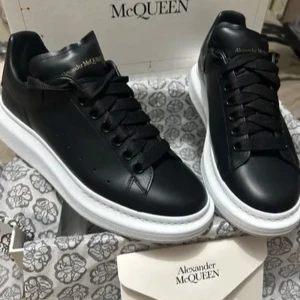 Svarta sneakers från Alexander McQueen - Snygga svarta sneakers från Alexander McQueen med vit sula och klassisk snörning. Skorna har en rund tå och är tillverkade i skinn, vilket ger en lyxig känsla. Perfekta för att lyfta vilken outfit som helst.