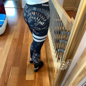 Mönstrade träningsbyxor från stronger - Snygga leggings med ett unikt mönster i svart, orange och vitt. De har en tight passform och vita ränder runt låret som ger en cool kontrast. Perfekta för träning.