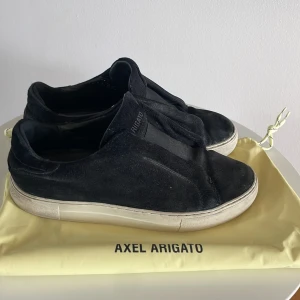 Svarta sneakers från Axel Arigato - Snygga svarta sneakers från Axel Arigato i mocka med en stilren design. Skorna har en vit sula och är perfekta för en avslappnad stil. De kommer med en praktisk dustbag för förvaring.