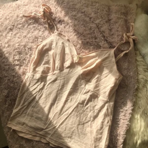 🎀Puderrosa linnetopp med rosett🎀 - Söt puderdosa linnetopp med smala axelband som knyts i rosetter. Toppen har en liten vit dekorativ rosett framtill och är perfekt för varma dagar eller att ha som pyjamaströja🌸🎀❣️