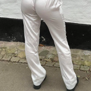 Vita byxor från Design by si - Snygga vita byxor från  designbysi  i ett glansigt material. Byxorna har en loose passform och är lågmidjade. Använt endast en gång 