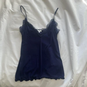 Mörkblå linnetopp från Amisu - Snygg mörkblå linnetopp från Amisu med spetsdetaljer vid halsringningen. Toppen har smala axelband och en ribbad struktur som ger en stilren look. Perfekt för att lägga till en touch av elegans i din garderob.