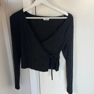 Mörkgrå omlottopp  - Snygg mörkgrå omlottopp  med långa ärmar och knytning i sidan. Perfekt för en stilren look. Passar bra till både jeans och kjol.
