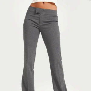 Grå kostymbyxor - Snygga grå kostymbyxor med hög midja och bootcut-stil. Perfekta för en stilren look. Byxorna har en diskret dragkedja framtill.