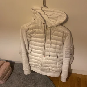 Vit quiltad hoodie med dragkedja - Säljer en stilren vit quiltad hoodie med dragkedja och huva. Tröjan har långa ärmar och ribbade muddar. Perfekt för vår eller sommar dagar. Hör av dig vid intresse!