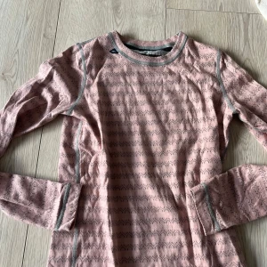 Rosa underställ från Devold - Säljer en rosa underställ från Devold med ett subtilt mönster. Tröjan har grå sömmar och är perfekt för kyligare dagar. Den är tillverkad i ett mjukt och bekvämt material.🩷🩷