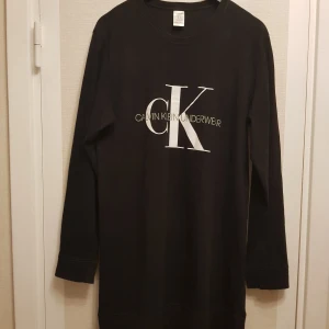 Svart långärmad tröja från Calvin Klein - Säljer en stilren svart långärmad tröja från Calvin Klein med stort CK-tryck på framsidan. Tröjan är tillverkad i mjuk bomull och passar perfekt för en avslappnad look.