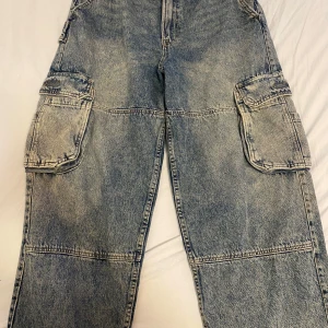 Blå cargopants från Bershka - Säljer ett par blå cargopants från Bershka i denim. Byxorna har stora fickor på sidorna och en avslappnad passform. Perfekta för en casual look.