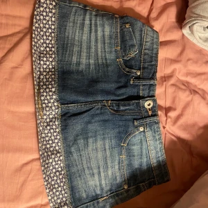 Jeanskjol med blommigt mönster - Snygg jeanskjol med en unik blommig kant i vitt och blått. Kjolen har klassiska femficksdetaljer och en knappstängning framtill. Perfekt för en avslappnad stil med en twist.