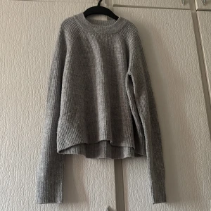 Grå ribbad tröja från H&M - Säljer en stilren grå ribbad tröja från H&M. Tröjan har en rund halsringning och långa ärmar, perfekt för kyligare dagar. Den är mjuk och bekväm, idealisk för en avslappnad look.