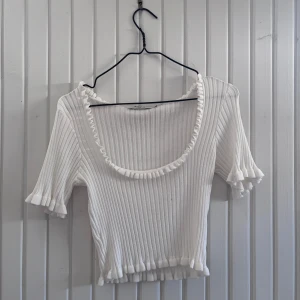 Vit ribbad topp - Säljer en söt vit ribbad topp med korta ärmar och volangdetaljer vid halsringning och ärmslut. Superfin🫶🏻