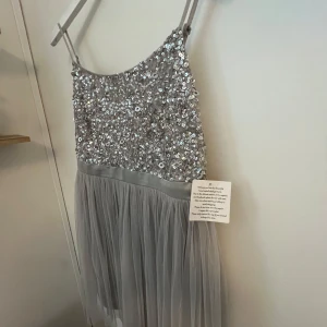 Grå paljettklänning storlek 40 - Supersöt klänning med paljetter och en rosett baktill. Aldrig använd och prislapp kvar. köpt på Asos och tillhör deras serie Maya. Nypris 1019kr