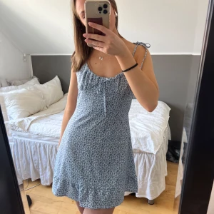 Blommig sommarklänning med knytband - Söt blommig klänning i ljusblått med små blommor. Klänningen har smala axelband med knytning och en lätt volangdetalj nedtill. Perfekt för varma sommardagar! Klänningen är knappt använd🌟🌟