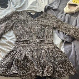 Leopardmönstrad klänning från Gina Tricot - Snygg leopardmönstrad klänning från Gina Tricot med volangdetaljer och v-ringning. Klänningen har långa ärmar och en smickrande passform som passar perfekt för en trendig look. Bara använd 1 gång 