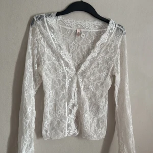 Vit spetstopp från Nelly - Säljer en elegant vit spetstopp från Nelly. Toppen har ett vackert blommönster och långa ärmar. Perfekt för att lägga till en romantisk touch till din outfit. 💫