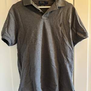Säljer en stilren grå pikétröja från Ralph Lauren med klassisk krage och broderad logga på bröstet. Perfekt för en avslappnad men ändå snygg look. Tröjan är kortärmad och gjord i stretchigt material för extra komfort.