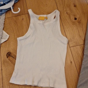 Linne - Säljer en vit ribbad linnetopp från Gina Tricot. Toppen har en enkel och stilren design med ärmlös skärning och rund hals. Perfekt för varma dagar eller som lager under en tröja.