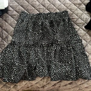 Svart prickig kjol - Säljer en svart kjol med vita prickar. Kjolen har en volangdetalj och elastisk midja för en bekväm passform. Perfekt för att ge en lekfull touch till din outfit.