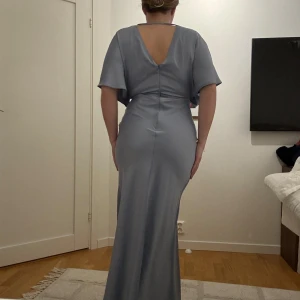 Ljusblå balklänning  - Oanvänd Ljusblå balklänning med omlott-design och slits framtill. Lite öppen i ryggen. Verkligen så fin! Storlek 38! Nypris 1300kr