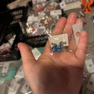 Blå tärningsörhängen - Snygga örhängen med blå tärningar som hänger från en metallring. Perfekta för att ge en lekfull touch till din stil. De är små och lätta, vilket gör dem bekväma att bära hela dagen.