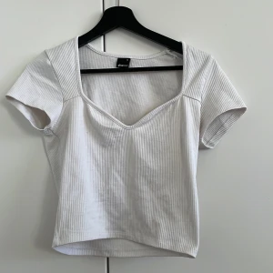 Vit ribbad topp - Säljer en vit ribbad topp med korta ärmar och en djup v-ringning. Perfekt för en stilren och enkel look. Toppen är i ett mjukt och stretchigt material.