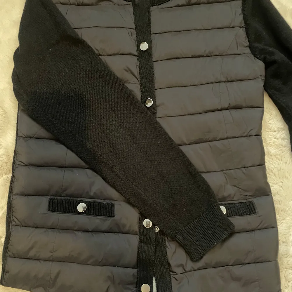 Snygg svart quiltad cardigan jacka med långa ärmar och knappar framtill. Jackan har en stilren design med ribbade detaljer vid ärmslut och nederkant. Perfekt för kyligare dagar. Passar s/m. Takit.