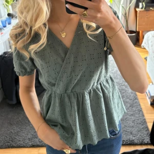 Grön omlottblus - Säljer en söt grön omlottblus med korta ärmar och spetsdetaljer. Fint skick