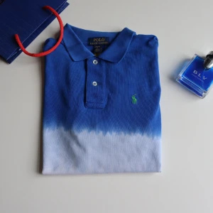  pikétröja från Ralph Lauren -  pikétröja från Ralph Lauren i blått, vitt och orange med en grön broderad logga på bröstet. en klassisk krage och knappar framtill. Den är nästan helt ny 