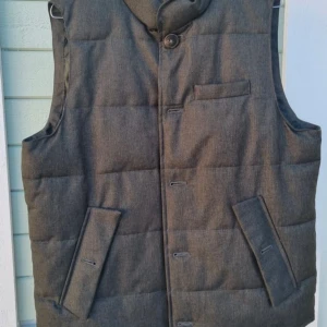 Väst från John Henric - Snygg grå quiltad väst från John Henric med knappar och praktiska fickor. Perfekt för lager-på-lager. Klassisk design som funkar till många stilar.