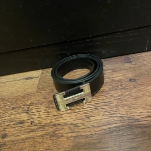 Svart bälte med guldfärgat spänne - Snyggt svart bälte med ett stilrent guldfärgat spänne i metall. Perfekt för att ge en elegant touch till din outfit. Passar både till jeans och kostymbyxor.