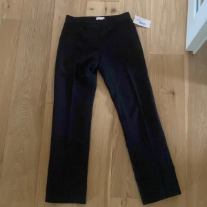 Svarta lågmidjade byxor från Nelly - Snygga svarta lågmidjade byxor från Nelly med raka ben. Perfekta för en stilren look. Byxorna har en enkel design med hällor för bälte och en diskret bakficka. Passar utmärkt för både vardag och mer uppklädda tillfällen. Dom är helt oanvända 