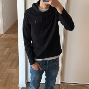 Svart hoodie från Ralph Lauren - Tja! 🌊,Säljer en stilren svart hoodie från Ralph Lauren med en liten röd logga på bröstet. Tröjan har långa ärmar och en praktisk huva med snörning. Perfekt för våren. Storleken är S och sitter fantastiskt. Modellen är 180cm lång