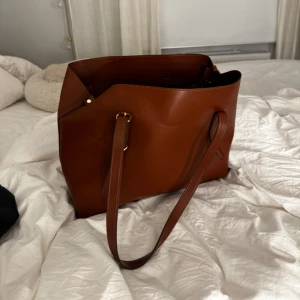 Brun axelväska i skinn - Snygg och rymlig brun axelväska i skinn med praktisk dragkedja. Perfekt för att bära med sig allt man behöver under dagen. Stilren design med långa axelremmar för bekväm användning.